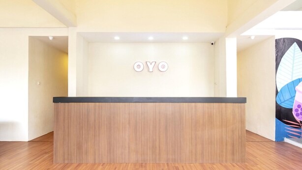 En receptionsdisk med träimitation och en svart skiva, en väggmonterad skylt med bokstäverna ”OYO” och en del av ett färgstarkt konstverk syns på höger sida.