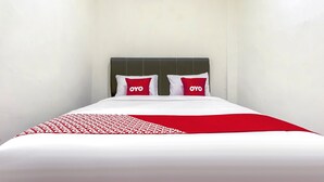En säng med ett vitt och rött sängöverkast, två kuddar med logotypen ”OYO”, och en mörk sänggavel.