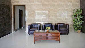 Un hall d’entrée avec un mur de marbre, des fauteuils en cuir, une table basse en bois et une plante en pot.