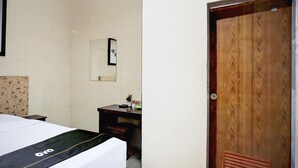 Une chambre d’hôtel avec un lit, une porte en bois, un miroir et un petit bureau agrémenté d’un vase de fleurs.