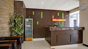 Zona de recepción de hotel con mostrador, un reloj y letrero de recepción.