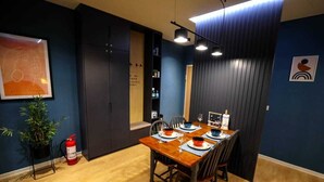 A dining area with a wooden table set for four, a fire extinguisher, and a potted plant. - Arkle Apartment 9 (Tirana)