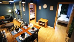 A compact hotel room with a dining area, a bed, a clock, and a small shelf. - Arkle Apartment 9 (Tirana)