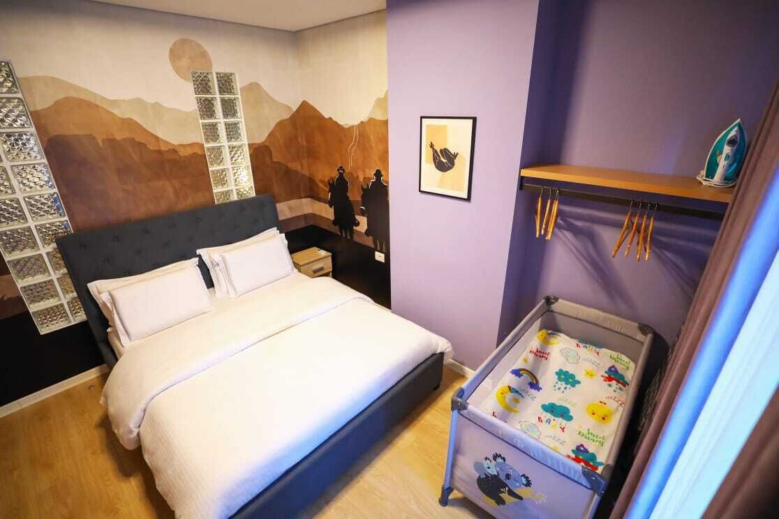 Une chambre à coucher avec un lit, une peinture murale, une étagère avec un fer à repasser et un berceau.