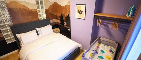 A bedroom with a bed, a wall mural, a shelf with an iron, and a baby crib.
