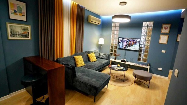A living room with a dark grey sofa, a wooden coffee table, a TV, and a bar area. - Arkle Apartment 9 (Tirana)