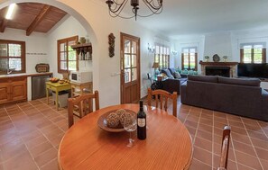 A dining area with a round table, chairs, a bottle of wine, and a bowl of fruit. - ES FIGUERAL SON RIBAS (Alaro)
