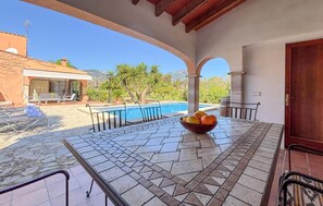 A covered outdoor area with a pool, a table with a bowl of fruit, and a view of a mountain. - ES FIGUERAL SON RIBAS (Alaro)