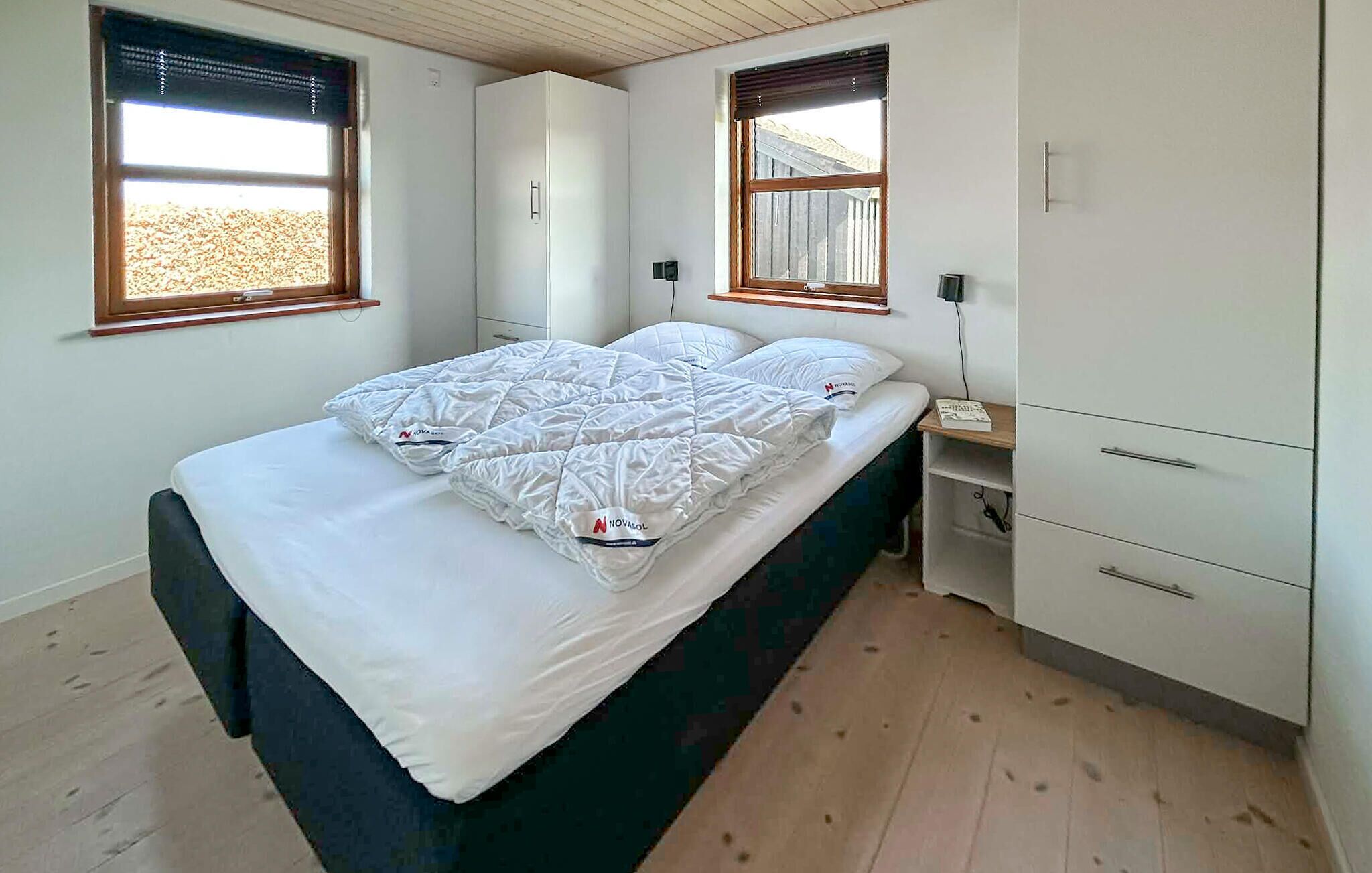 Ein Schlafzimmer mit einem Bett, zwei Fenstern, einem Kleiderschrank und einem Nachttisch.