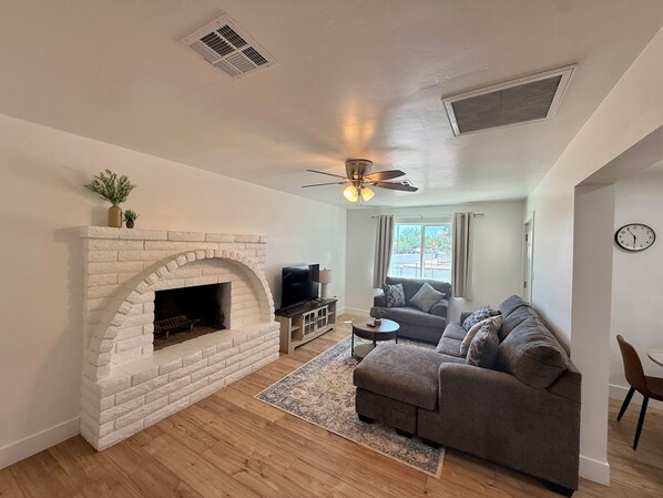 A living room with a fireplace, a ceiling fan, a sofa, and a TV. - Your Home Base in Safford Comfort + Convenience (Safford)