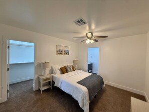 A bedroom with a bed, bedside tables, a ceiling fan, and a door. - Your Home Base in Safford Comfort + Convenience (Safford)