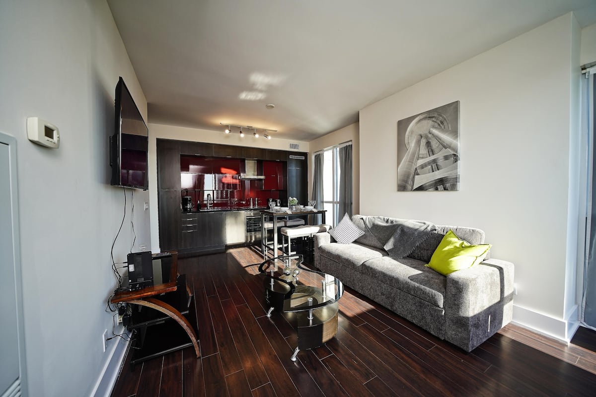 A modern living room with a grey sofa, a glass coffee table, and a dining area in the background.