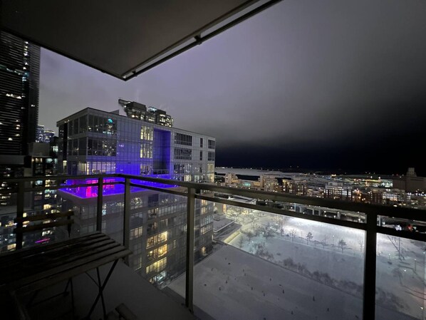 A high-rise building with a glass facade, a balcony with a blue-lit pool, and a view of the cityscape at night.