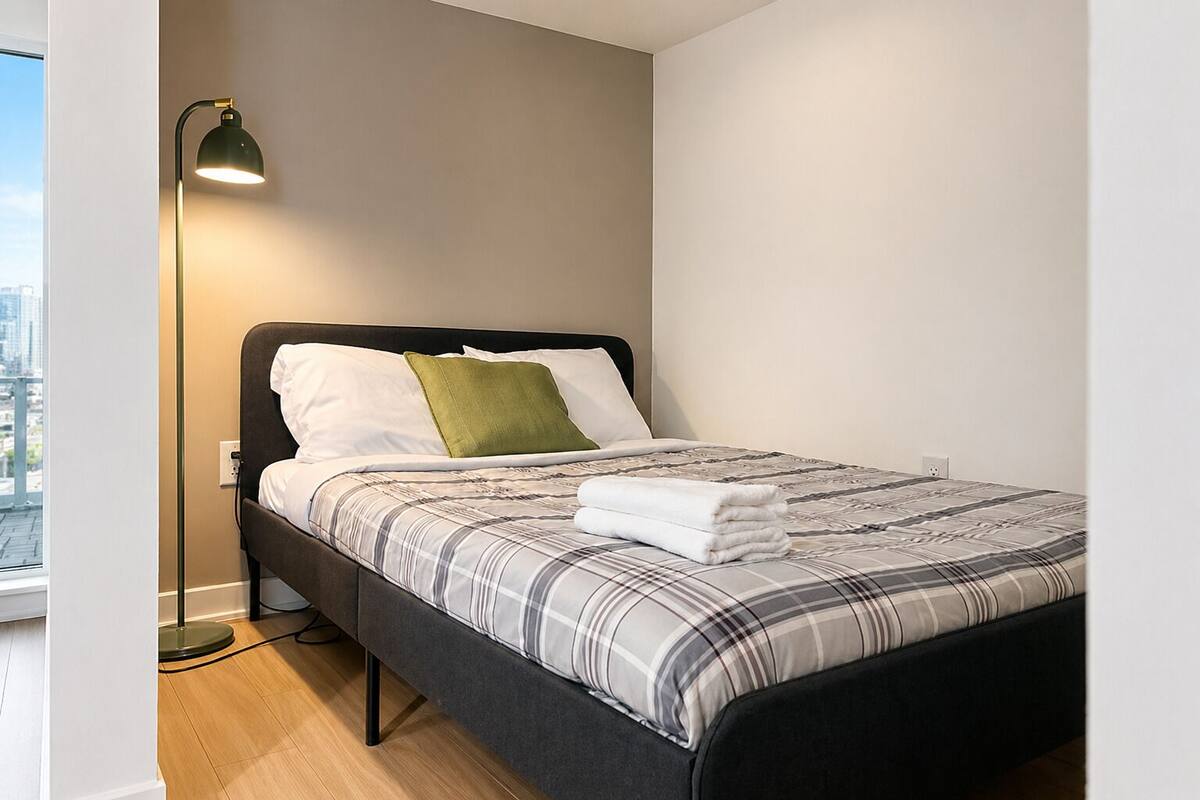 A neatly made bed with a plaid bedspread, a green pillow, and a black headboard.
