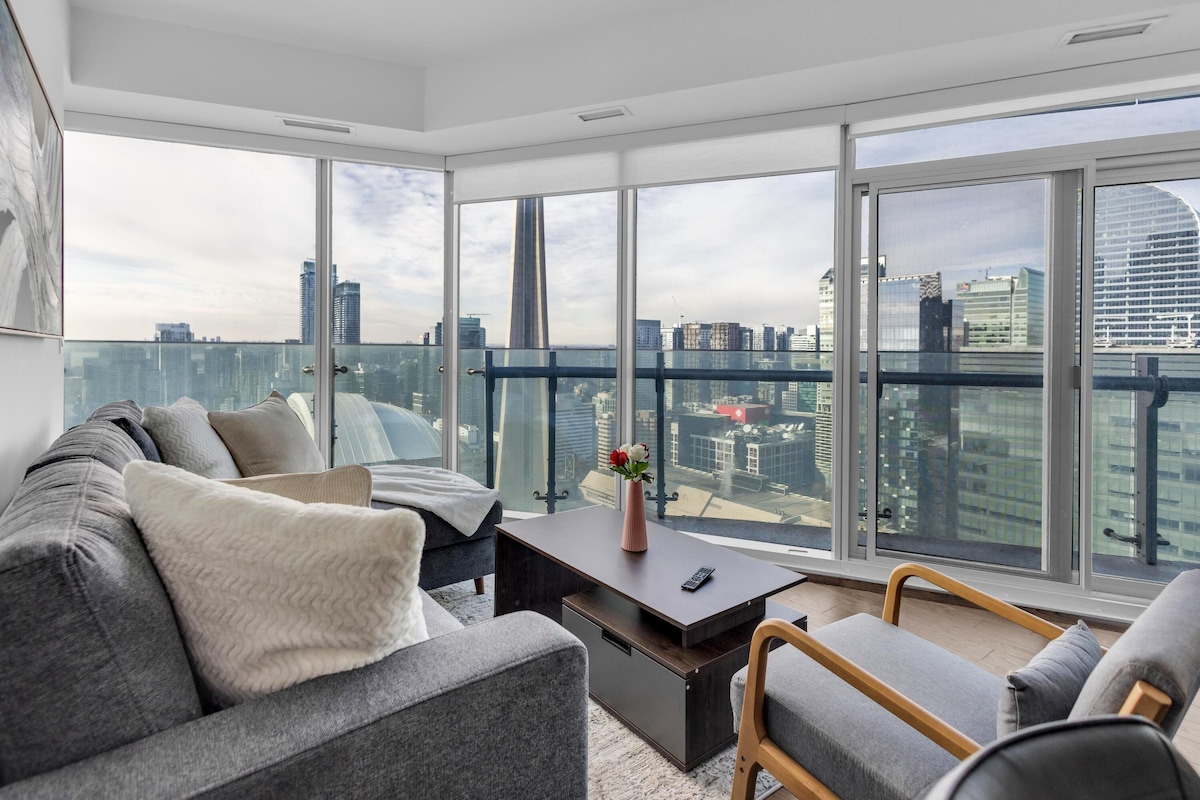 A modern living room with a sofa, a coffee table, and a view of a cityscape through large windows.