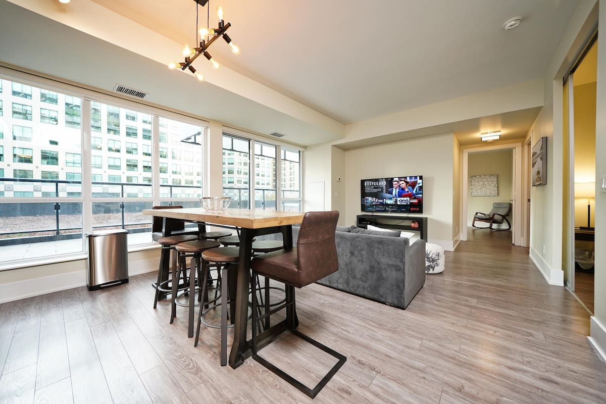 A modern living room with a dining area, large windows, a television, and a sofa.