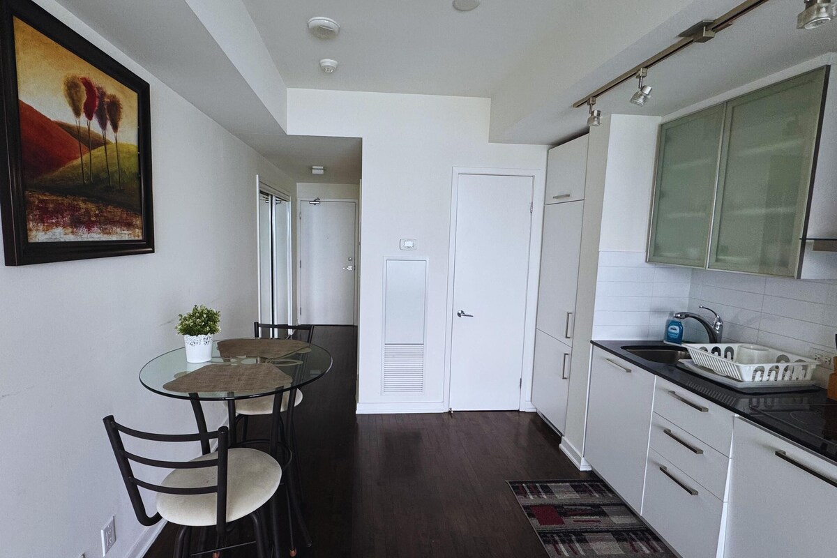 A compact kitchen with white cabinets, a black countertop, and a dining area with a glass table and chairs.