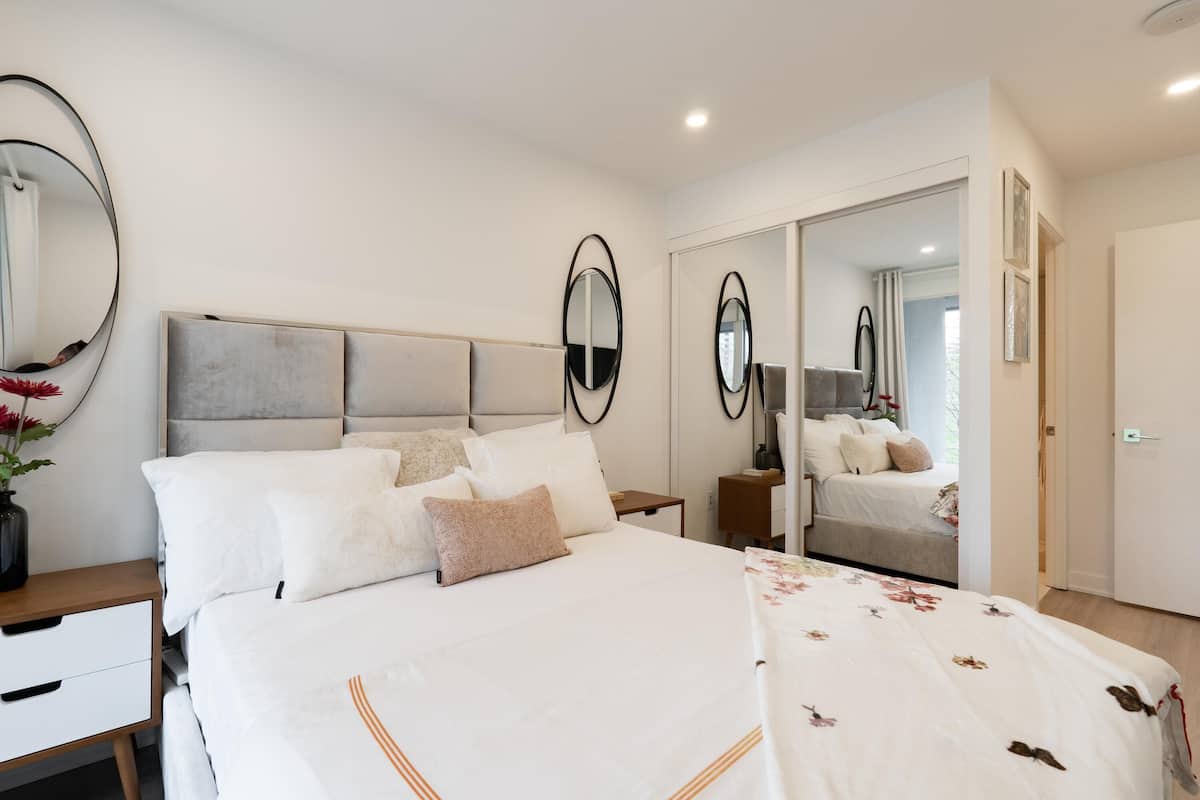 A modern bedroom with a large bed, a bedside table, a mirror, and a wardrobe.