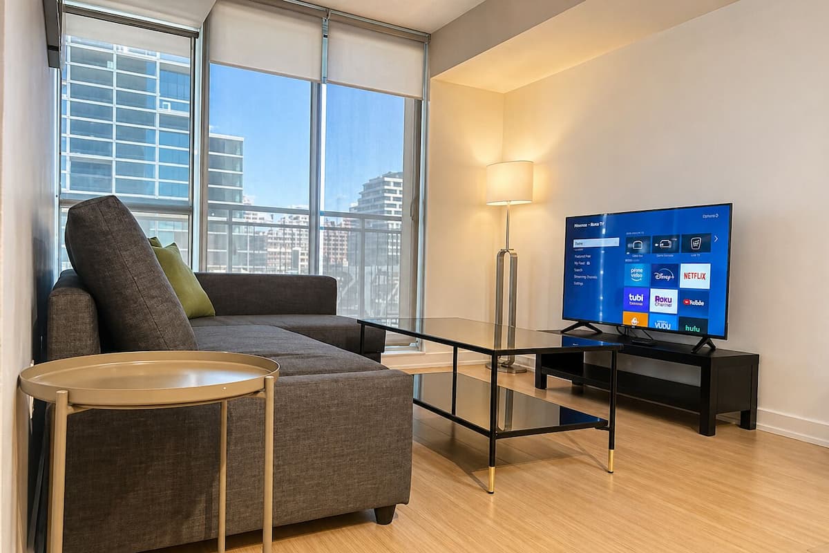 A modern living room with a sofa, a TV, a lamp, and a view of the city.