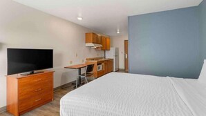 Een hotelkamer met een bed, een televisie, een bureau met stoel, een magnetron en een koelkast.