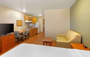 A hotel room with a bed, a TV, a desk with a chair, a kitchenette, and a sofa. - 1 King Bed | Hearing Accessible, Kitchen (Pelham)