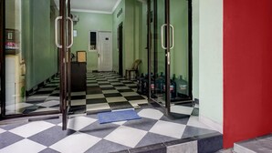 Eine Hotellobby mit Schachbrettmuster-Boden, Glastüren, einer blauen Matte und einer Reihe Wasserflaschen rechts.
