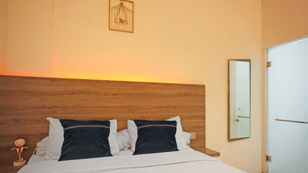 A hotel room with a wooden headboard, a bed with white and dark blue bedding, a small figurine on the nightstand, and a door with a mirror. - Cozy Double Escape W/ Free WiFi and Parking (Medan)