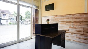 A reception desk with a stone wall, a television mounted above it, and a glass door leading outside.