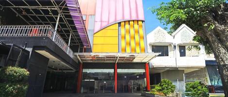 A modern building with a glass entrance, a covered area with a metal roof, and a tree to the right.