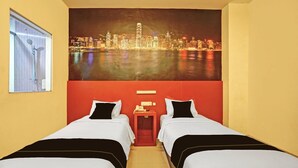 Ein Hotelzimmer mit zwei Betten, Blick auf die Stadtlandschaft, einem Fenster mit Jalousien und einer roten Akzentwand.