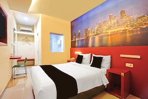 Ein Hotelzimmer mit Bett, einem Stadtbildgemälde, einer roten Akzentwand, einem kleinen Nachttisch und einem Sessel.