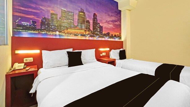 Ein Hotelzimmer mit einem großen Bett, zwei Nachttischen mit Lampen, einem Telefon und einem Stadtbild an der Wand.