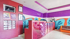 Ein Empfangsschalter mit violett-rosa Farbgestaltung, ein darüber befestigter Fernseher und ein gerahmtes Zertifikat an der Wand.
