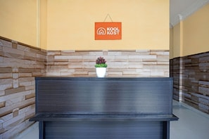 Una recepción con un cartel que dice 'Kool Kost', una planta en maceta sobre la mesa y una pared de piedra al fondo.