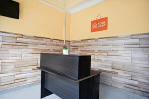 Un espace d’accueil avec un mur en pierre, un comptoir noir et une enseigne indiquant « KOOL KOST ».