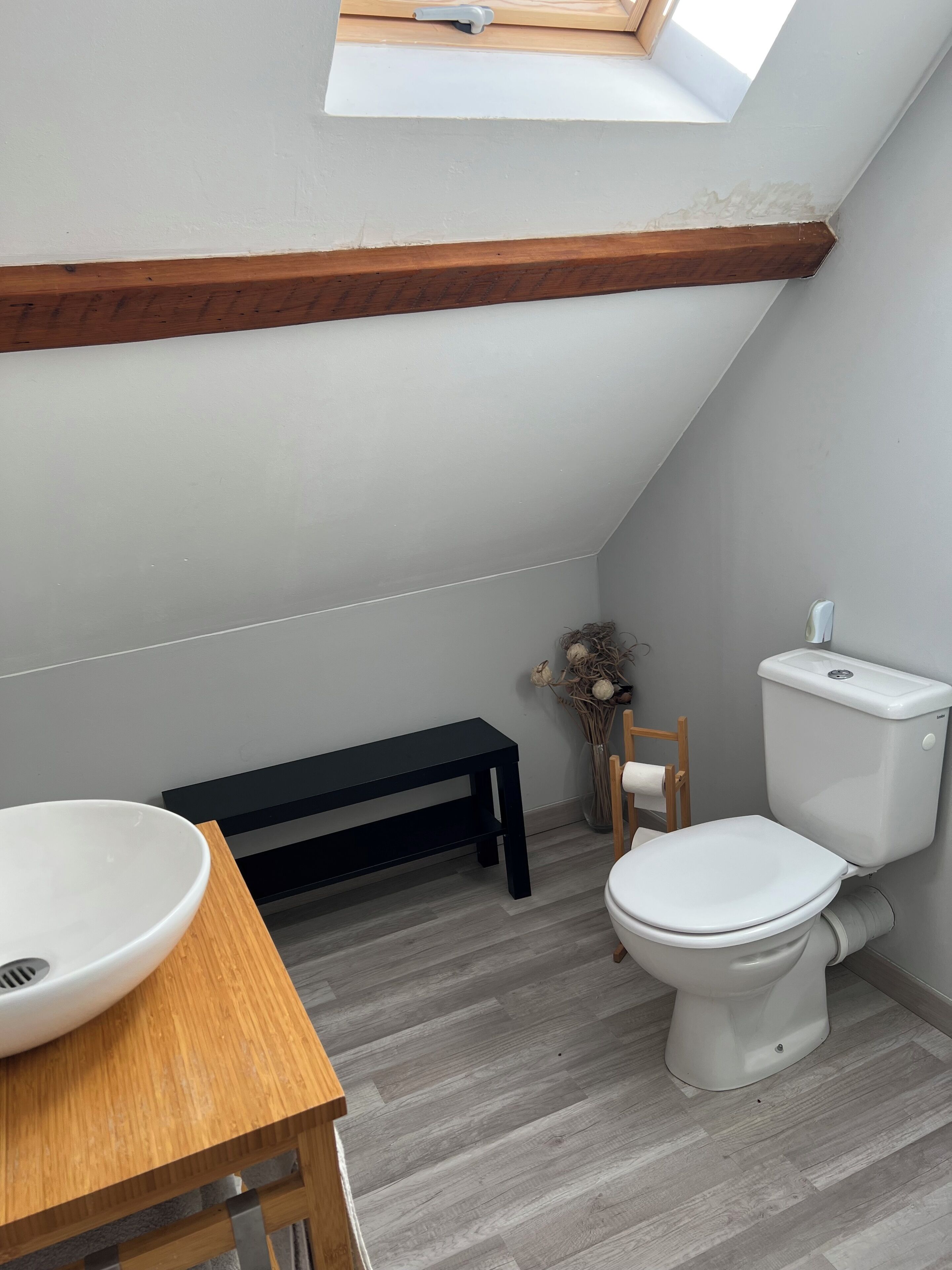 A small, modern bathroom with a skylight, a wooden bench, a toilet, and a sink.