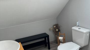 A small, modern bathroom with a skylight, a wooden bench, a toilet, and a sink.