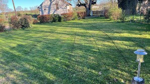 A stone house with a large tree in front, a well-maintained lawn, and a metal lamp post.
