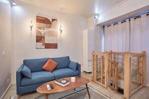 A modern room with a blue sofa, a wooden coffee table, a wall-mounted abstract art piece, and a wooden rack with glass doors. - Charming Duplex Center of Paris (Paris)