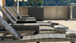 Outdoor lounge chairs, a small tree, and a view of a forested mountain range. - Villa in Tyrol with pool (Stanz bei Landeck)