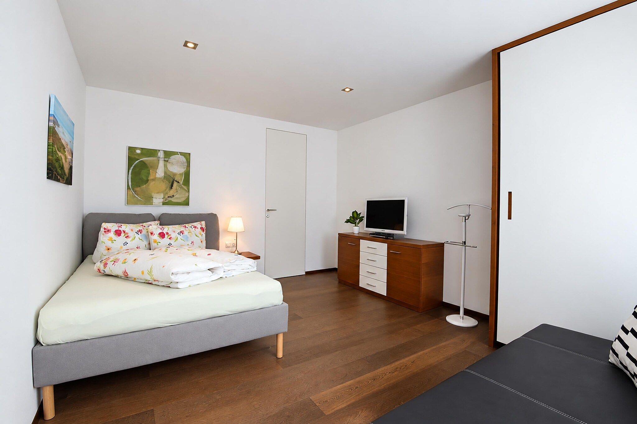 A bedroom with a bed, bedside table, lamp, TV, and a desk with a chair.
