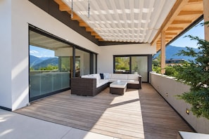 A modern outdoor living space with a wooden deck, built-in seating, and large sliding glass doors offering mountain views.