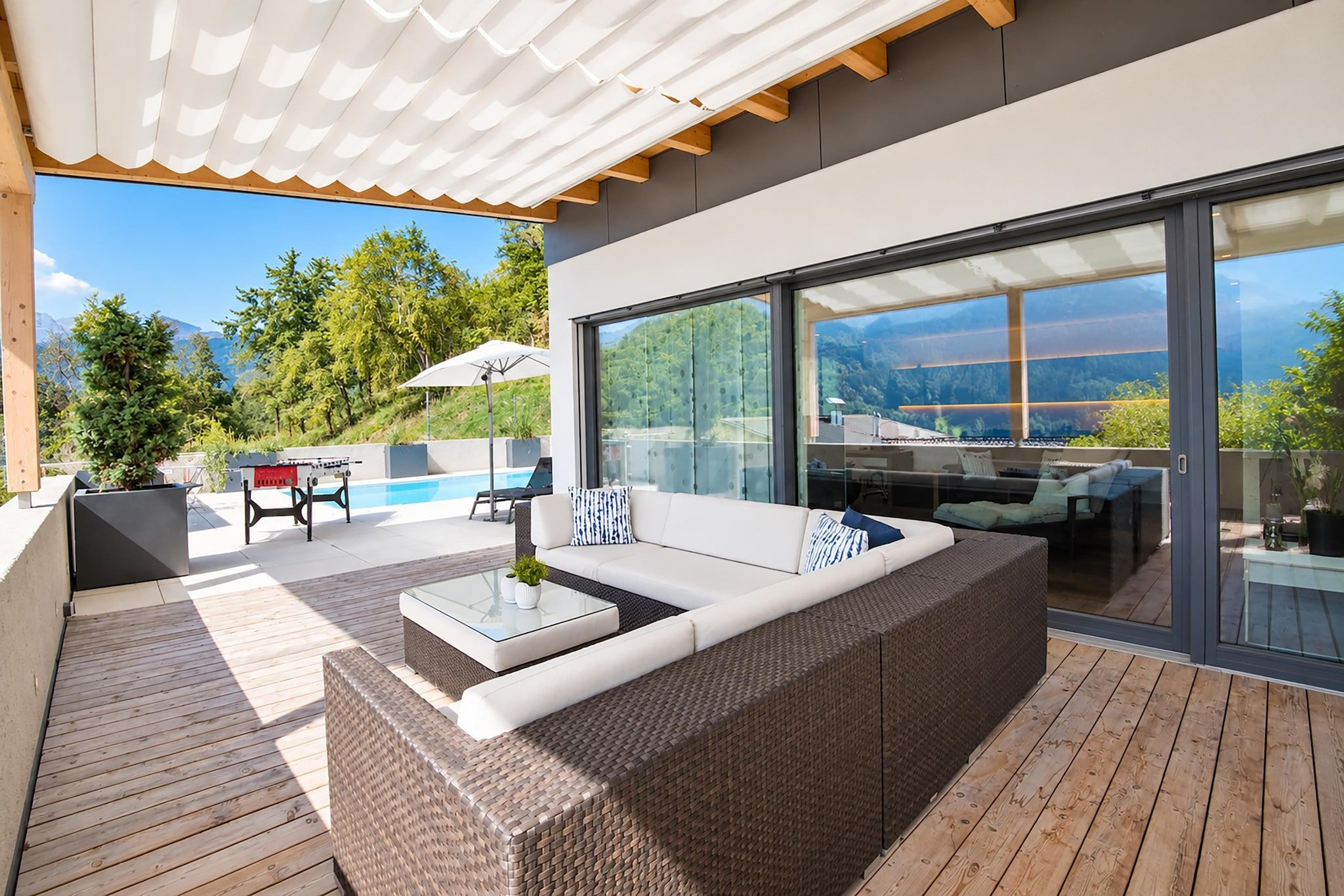 A modern outdoor living area with a sofa, a glass table, and a pool table.
