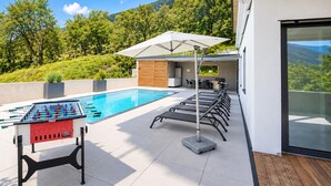 Un espace aménagé au bord de la piscine, comprenant une table de baby-foot, des chaises longues et un barbecue.