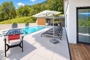 Un espace aménagé au bord de la piscine, comprenant une table de baby-foot, des chaises longues et un barbecue.