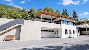 Une maison moderne à deux étages, dotée d’un espace extérieur couvert, d’un escalier et offrant une vue sur les montagnes.