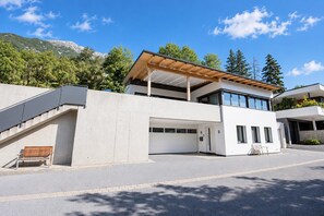 Une maison moderne à deux étages, dotée d’un espace extérieur couvert, d’un escalier et offrant une vue sur les montagnes.
