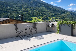 Una terraza en la azotea con piscina, dos sillas, una mesa y una fuente de agua.