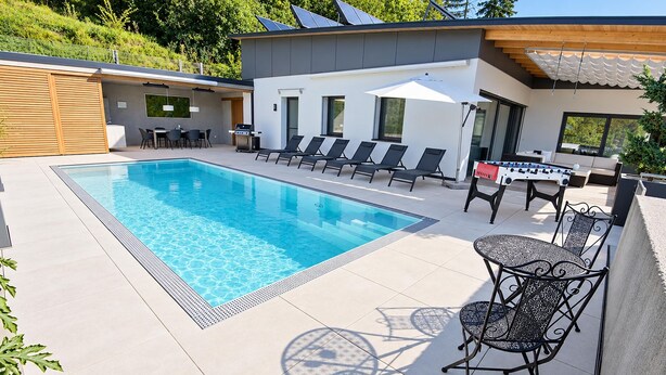 Un espace piscine extérieur moderne, doté d’une piscine à l’eau cristalline, de chaises longues, d  ’une table de baby-foot et d’un coin salon abrité.
