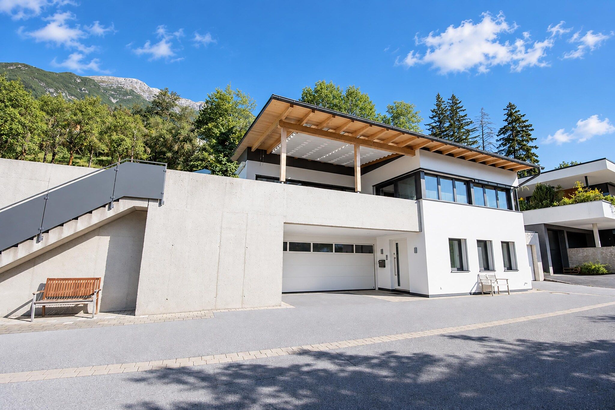 Une maison moderne à deux étages, dotée d’un espace extérieur couvert, d’un escalier et offrant une vue sur les montagnes.